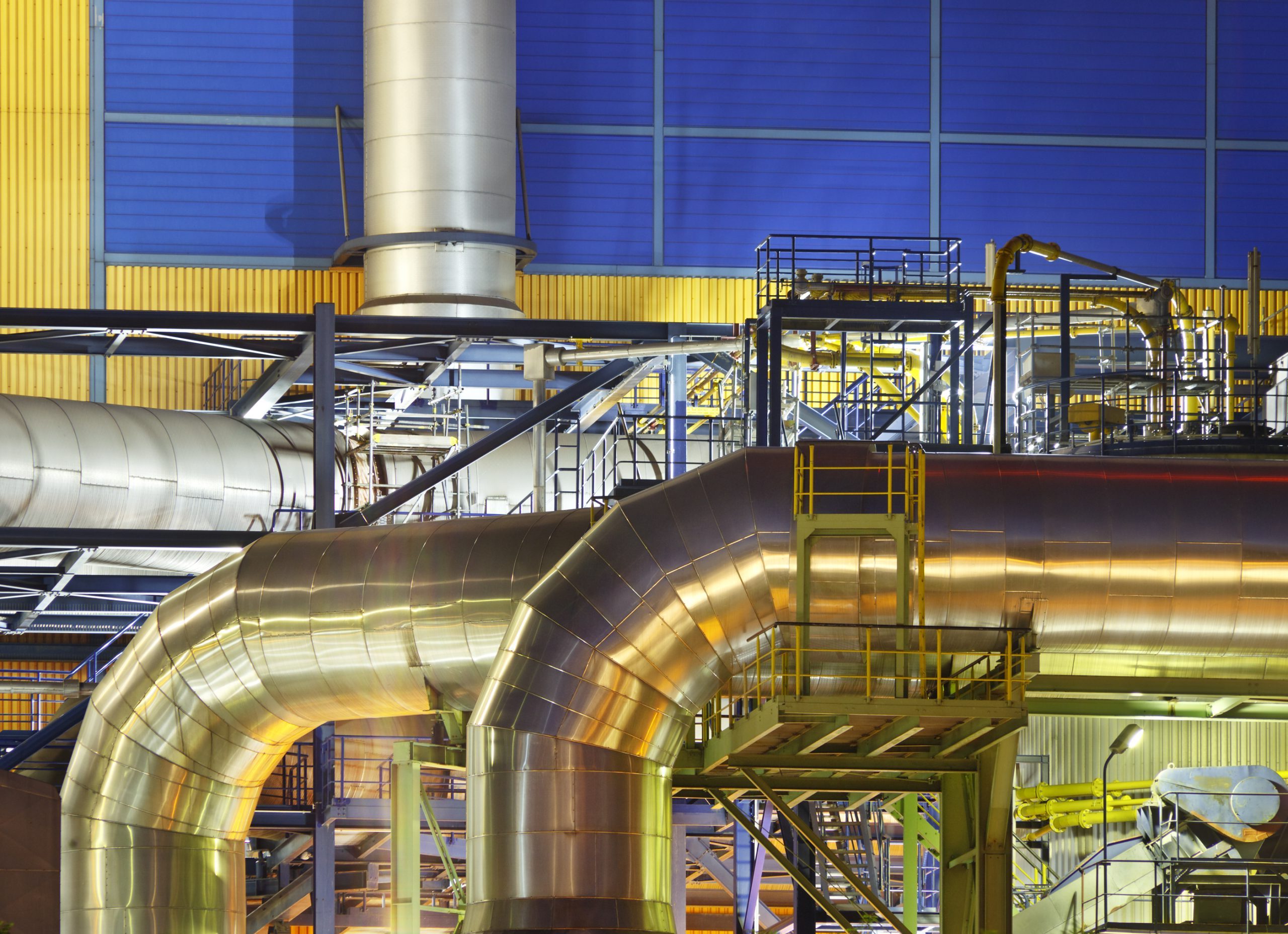 Large silver pipes of an incinerator plant at night. An incinerator plant at a canal with night blue sky.